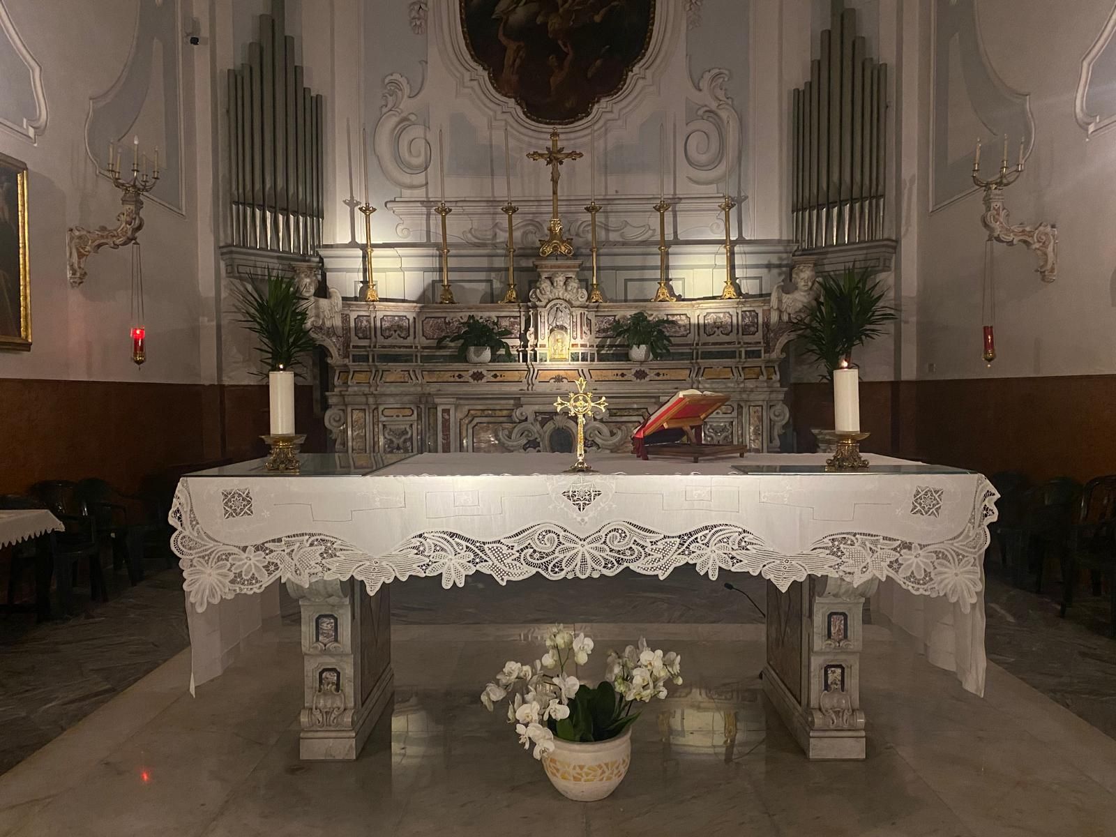 L'altare con la tovaglia ricamata, i candelieri dorati e un vaso di orchidee bianche.