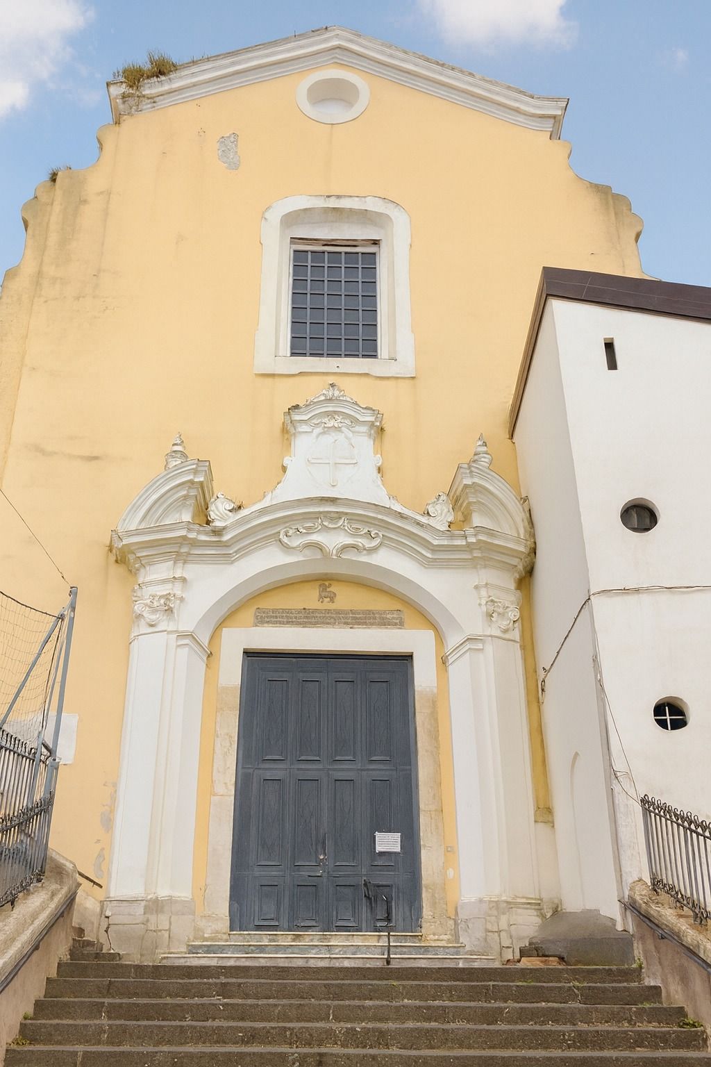 Il portale della chiesa: stucchi bianchi sull'intonaco giallo e il portone grigio.